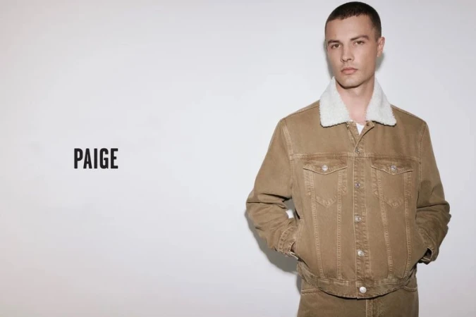 Model Will Verona wearing a tan denim shearling collar jacket and matching pants against a white background for Paige.