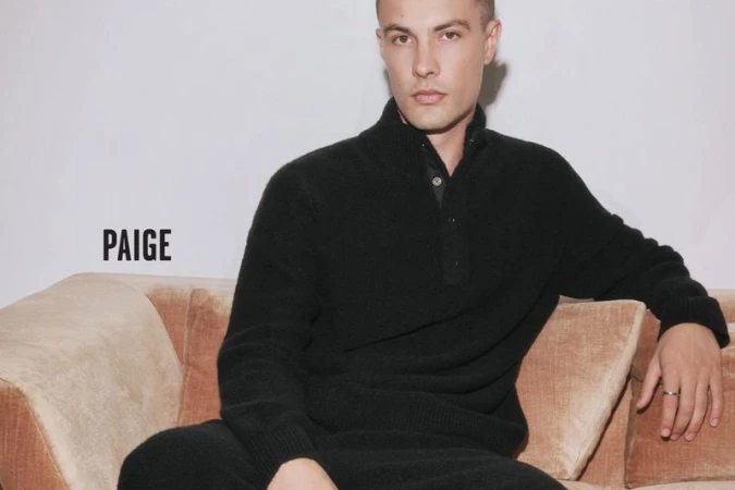 Model Will Verona wearing a black mock neck knit sweater seated on a tan velvet sofa for Paige.