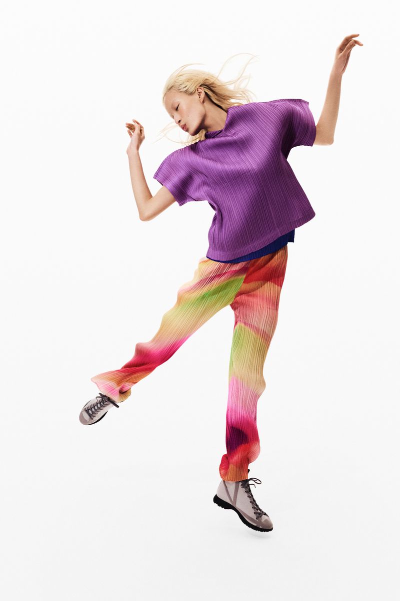 Fashionable woman in purple shirt and colorful pants mid-air against white background. Stylish attire for fashion and lifestyle context.