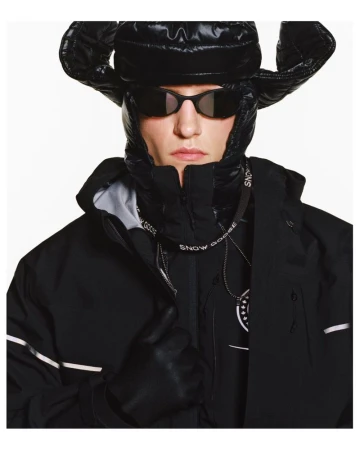 Fashionable adult male wearing black winter coat with fur-lined hood, black hat, sunglasses, and gloves, in a studio shot.