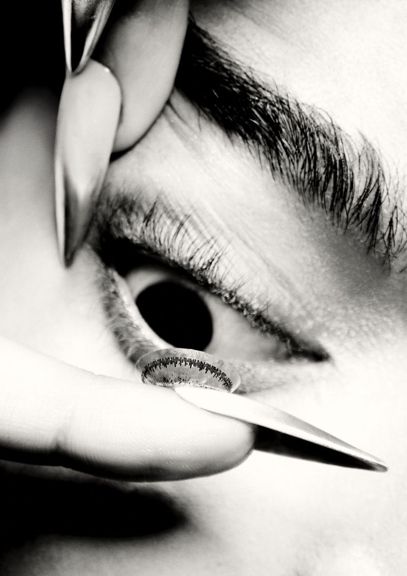 Close-up black and white shot shows a person's eye with a contact lens being inserted. Focus on the eye and contact.