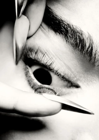 Close-up black and white shot shows a person's eye with a contact lens being inserted. Focus on the eye and contact.