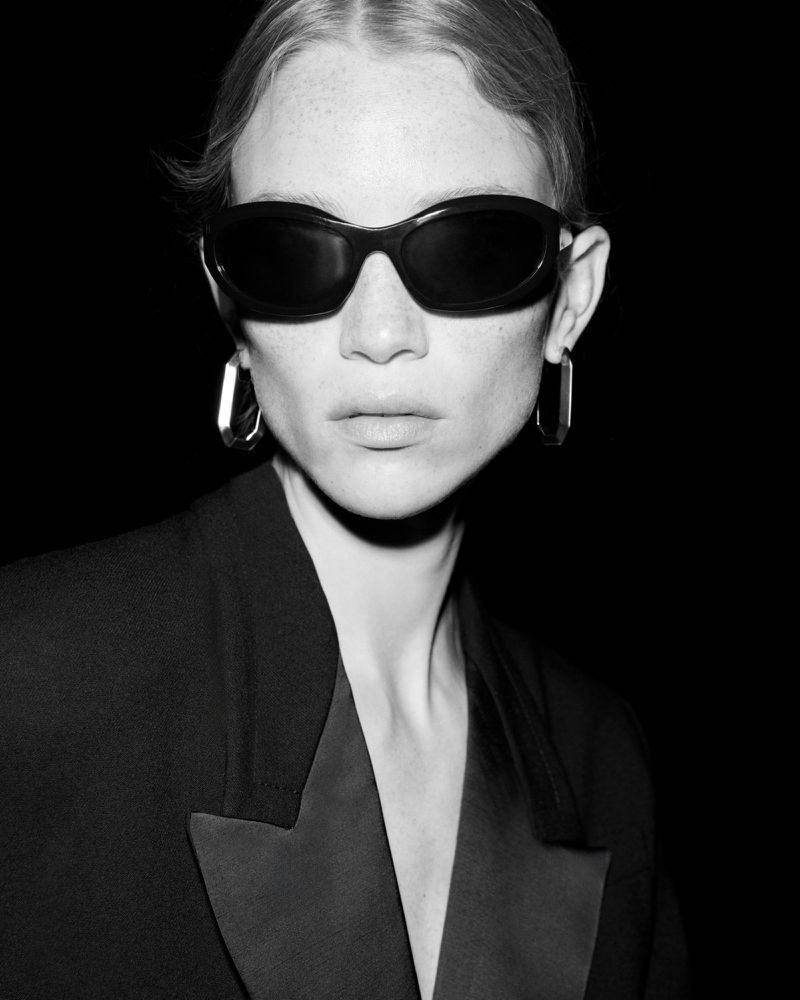 Close-up black and white portrait of a woman with fair skin wearing dark sunglasses and a black jacket with satin lapels.