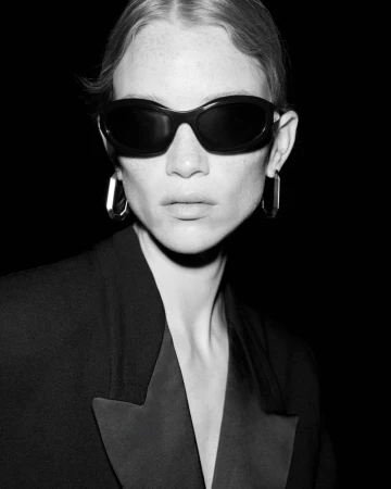 Close-up black and white portrait of a woman with fair skin wearing dark sunglasses and a black jacket with satin lapels.