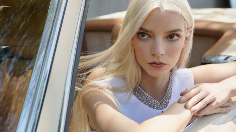Anya Taylor-Joy poses in a white dress inside a car, captured in a medium shot. The focus highlights her facial expression and platinum blonde hair.