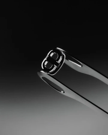 Close-up studio shot of chrome-toned nail clippers featuring logo detail, set against a gradient background in black and gray.