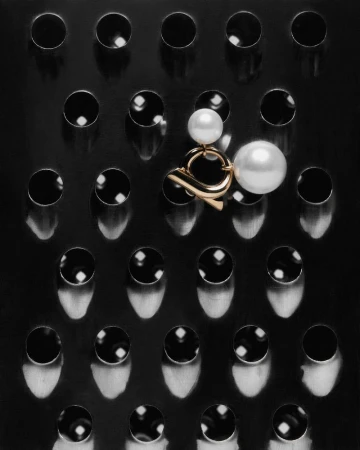 Overhead shot of gold and pearl earring on a black metal cheese grater, pearls reflecting light in a dark, minimalist studio product photo.