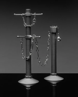 Silver chain jewelry and a spherical charm draped across two industrial threaded metal posts on a dark reflective surface.