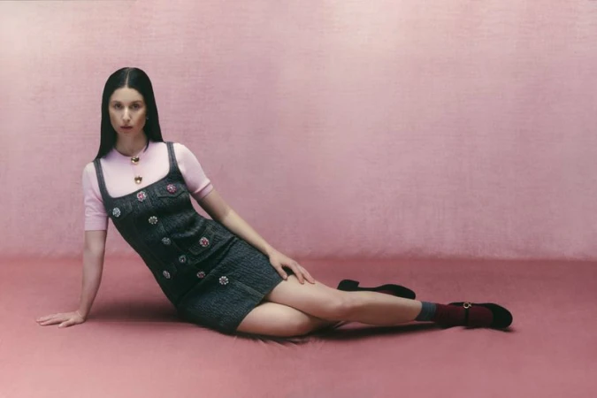 Woman in a denim dress posing against a pink backdrop. She's lying down, looking at the camera. The scene features a simple and clean aesthetic.