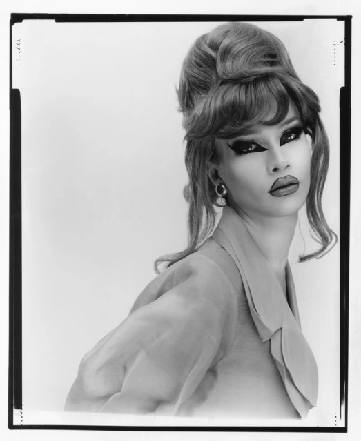Black and white portrait of a model with a beehive hairstyle, wearing a collared shirt against a plain background, in a studio.
