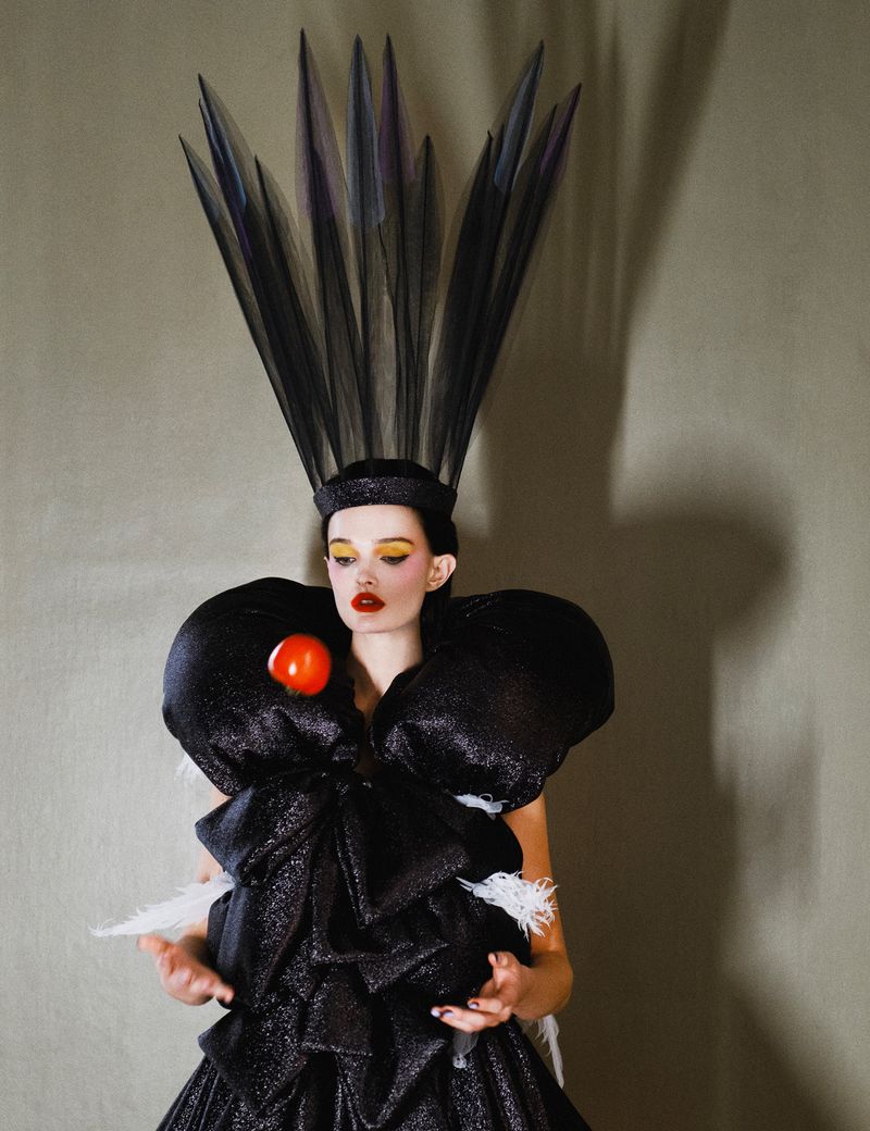 Woman wearing a black avant-garde gown and large feather headpiece posing in a studio with grey background, beauty and fashion.
