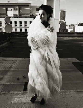 Monochrome portrait of a woman in a fur coat on a rooftop, with city buildings in the background, evoking high fashion and urban elegance.