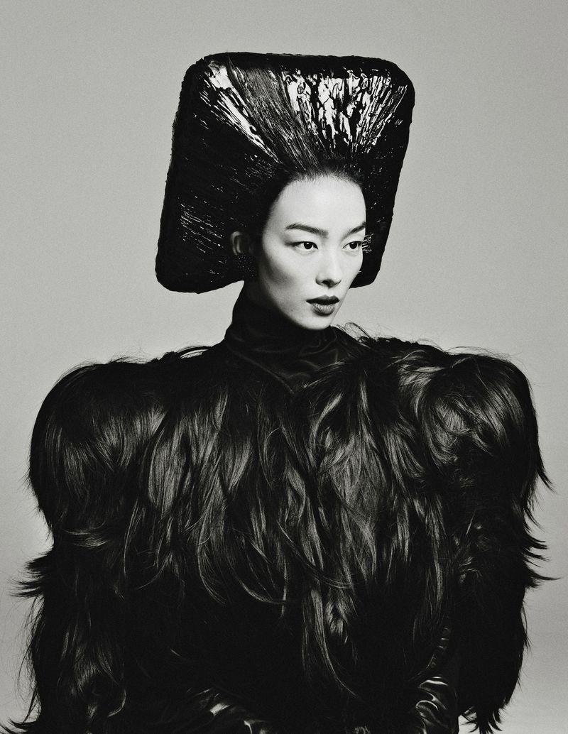 Model Fei Fei Sun wearing an avant-garde black sculpted square headdress and voluminous textured cape against a neutral studio backdrop.