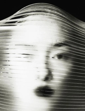Striking black-and-white portrait of a person's face obscured by parallel ribbons, creating an abstract, textured effect in studio.