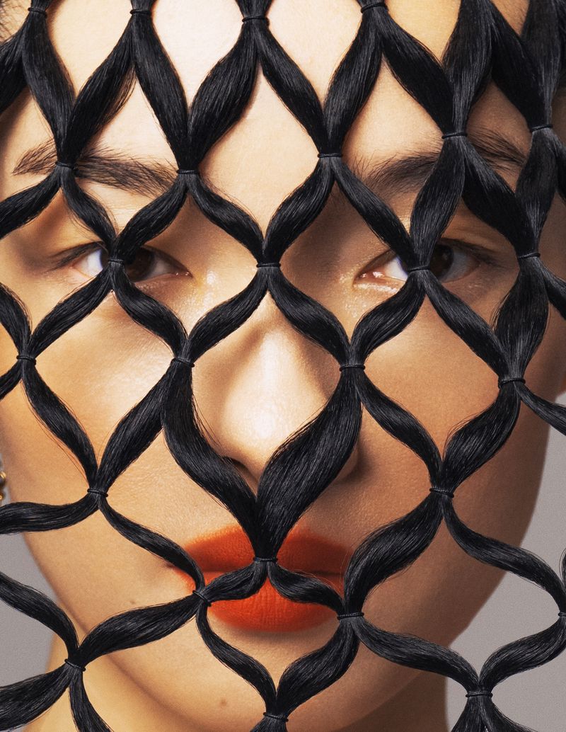 Close-up of a woman with a hair net design, bright orange lipstick, and a light skin tone.