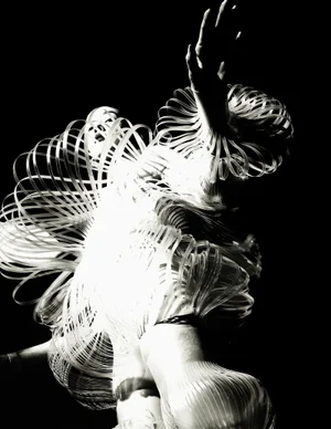 Model FeiFei Sun wears a sculptural avant-garde garment made of luminous coiled loops against a pitch black background.