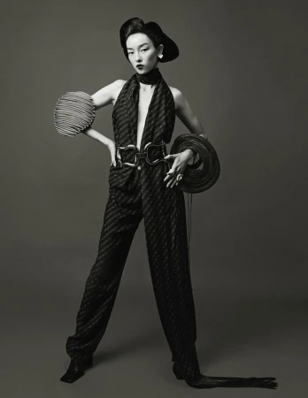 Model Fei Fei Sun posing in a dark halter jumpsuit with sculpted pleated accessories against a studio backdrop.