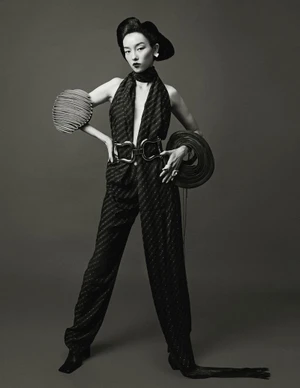 Model Fei Fei Sun posing in a dark halter jumpsuit with sculpted pleated accessories against a studio backdrop.