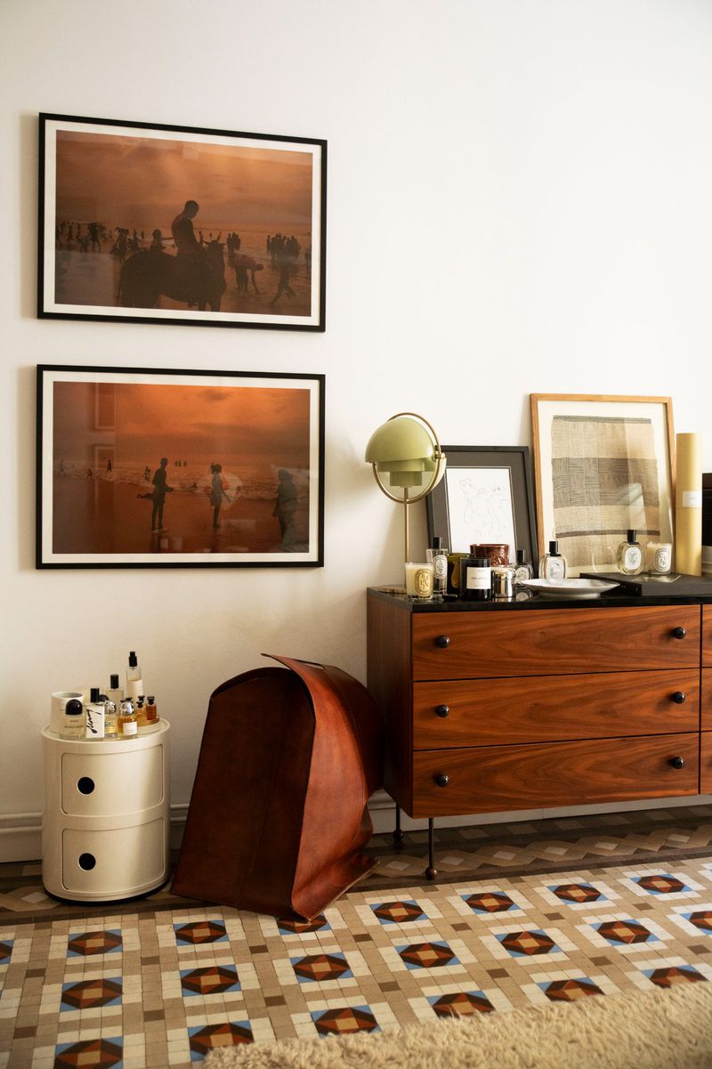 Interior shot of a room featuring mid-century modern furniture, including a wood dresser, side table, lamp, and decorative artworks.