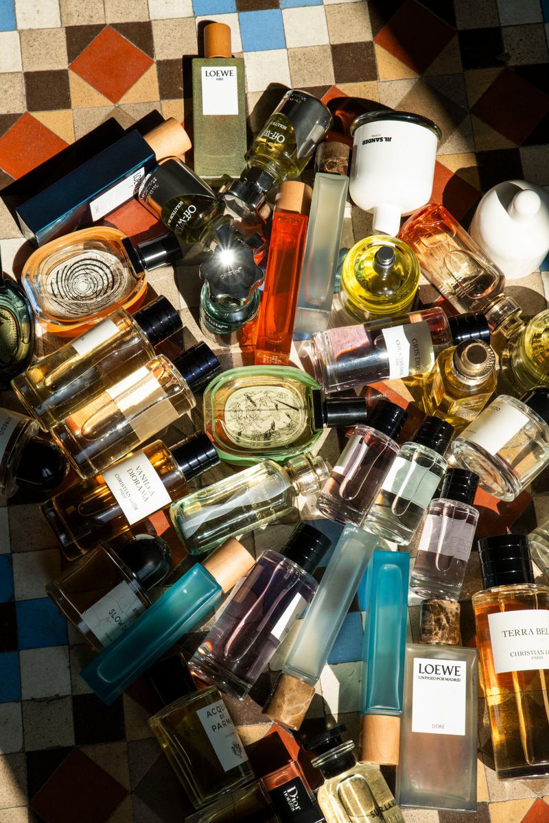 Overhead shot of assorted colorful glass perfume bottles in various shapes and sizes scattered on tiled surface with geometric pattern.