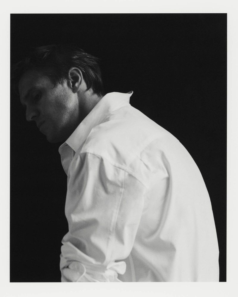 Monochrome portrait of an adult male in a white dress shirt against a dark backdrop, focusing on facial features and upper body.