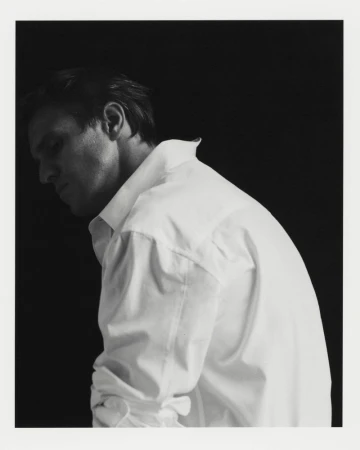 Monochrome portrait of an adult male in a white dress shirt against a dark backdrop, focusing on facial features and upper body.