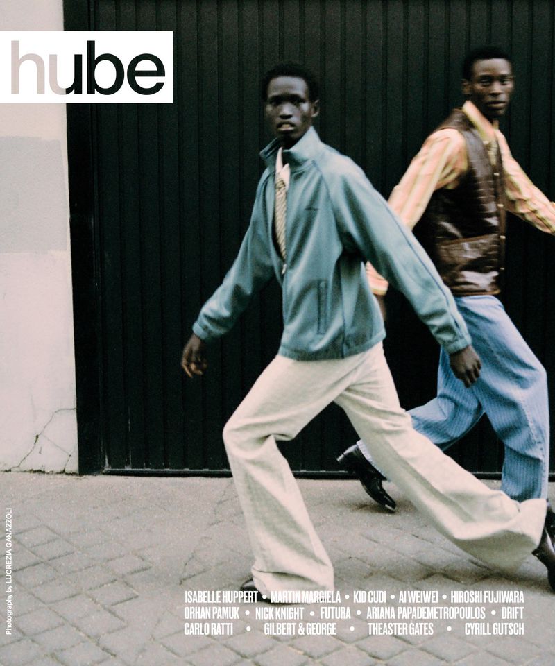 Two dark-skinned male fashion models walking outdoors in wide-leg trousers and vintage jackets, photographed for Hube Magazine.