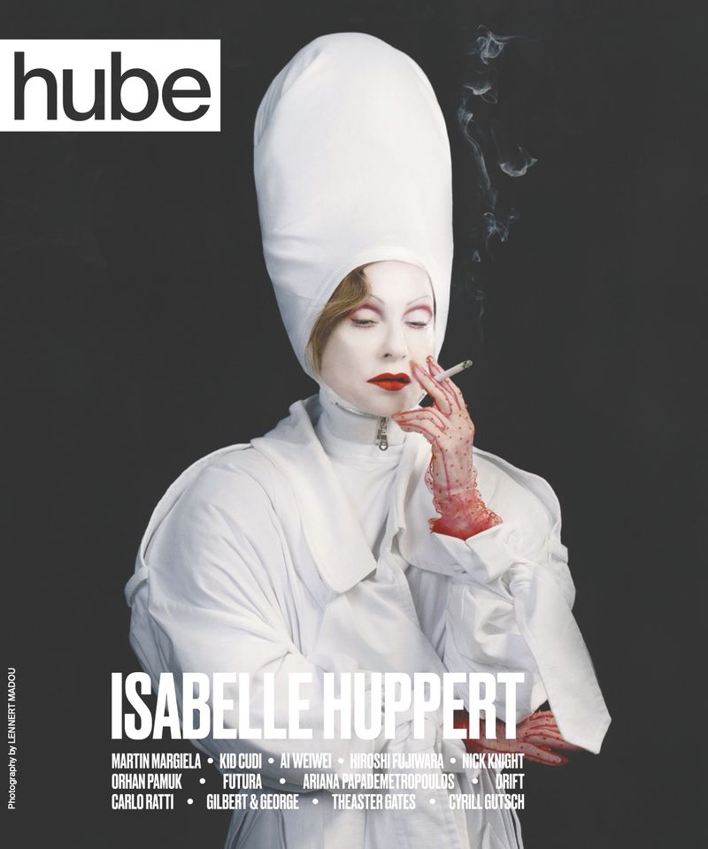Magazine cover featuring Isabelle Huppert in distinctive white headwear, smoking, with a grey backdrop and artistic elements.