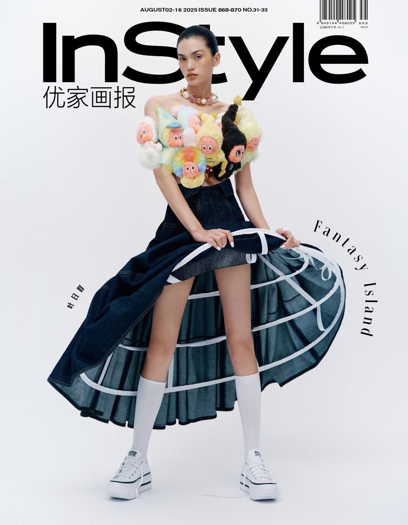 Magazine cover featuring a young woman in a denim skirt, platform shoes, and a top adorned with doll heads on a white backdrop.