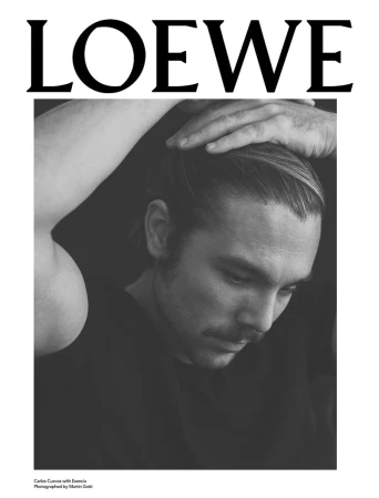 Black-and-white portrait of a fair-skinned adult male with a mustache, hand on his head, wearing a dark shirt, with 'LOEWE' text above.