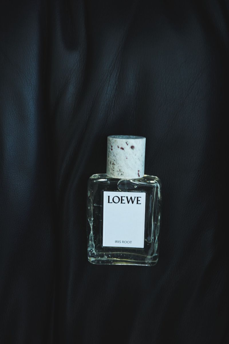 Close-up shot of a Loewe Iris Root perfume bottle against a dark, textured background, highlighting the bottle's design and the brand's label.