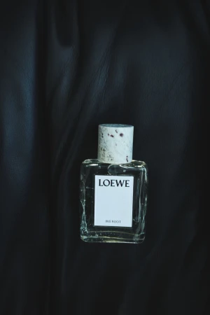 Close-up shot of a Loewe Iris Root perfume bottle against a dark, textured background, highlighting the bottle's design and the brand's label.