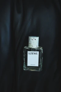 Loewe Iris Root perfume bottle with a speckled textured cap resting on draped black fabric.