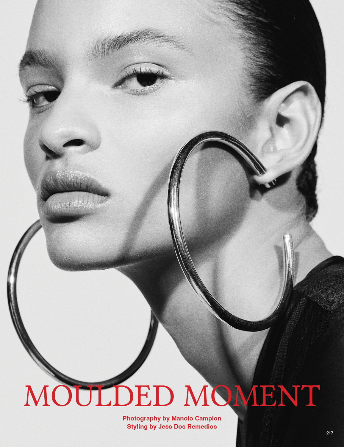 Close-up black and white portrait of a woman with large hoop earrings, highlighting beauty and fashion in a minimalist studio setting.