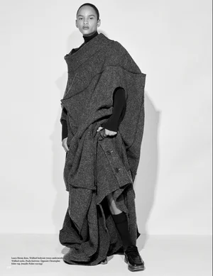 Model wearing a voluminous dark textured wool coat over a black turtleneck against a plain white background