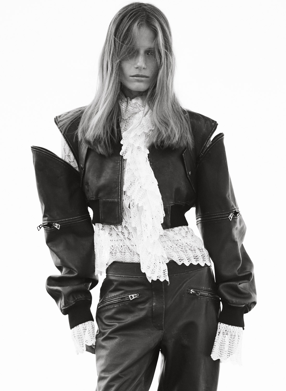 Black and white portrait of a woman wearing a black leather jacket and pants paired with a white lace top in a photo studio.