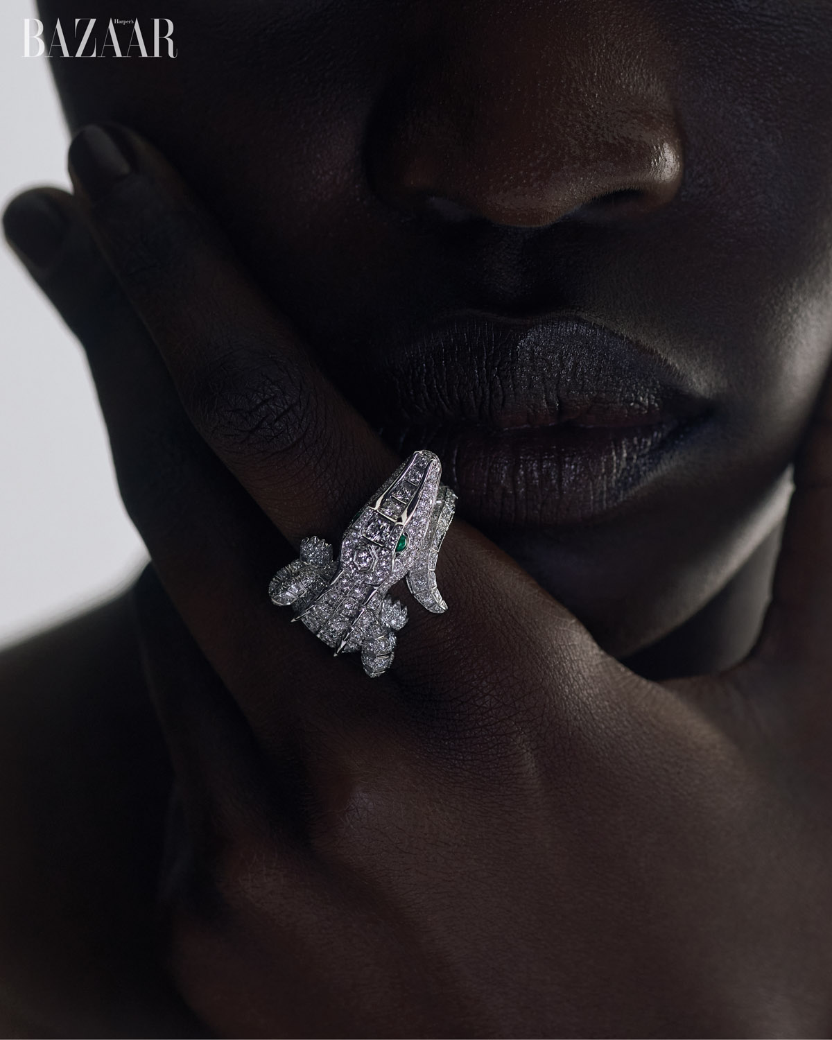 Close-up of a dark-skinned person's face and hands, showcasing a detailed crocodile-shaped ring adorned with diamonds, emphasizing luxury jewelry.