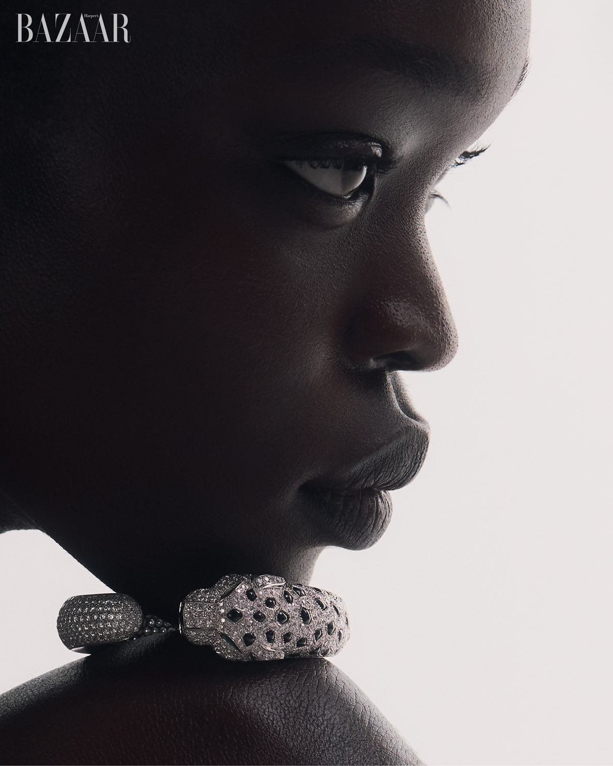 Close-up profile of a Black woman wearing a statement diamond panther necklace against a bright white background in a fashion editorial setting.
