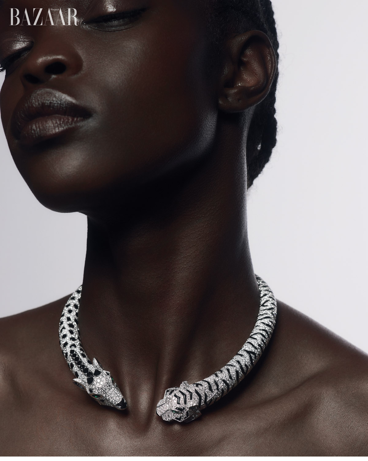 Close-up of dark-skinned woman wearing tiger-motif necklace against a light gray backdrop, promoting Harper's Bazaar.