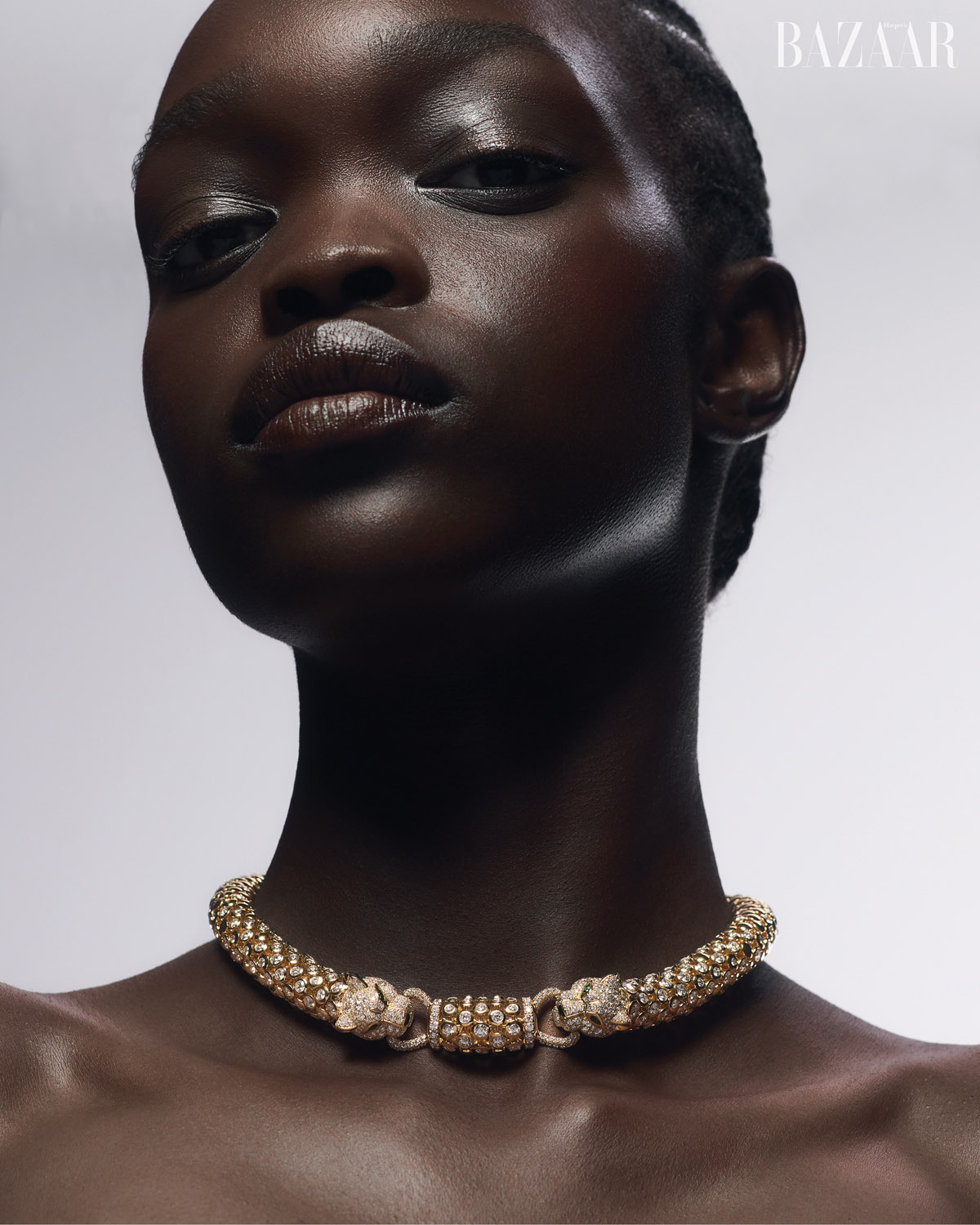 Close-up of a Black female fashion model wearing an ornate gold choker necklace with two jeweled tiger heads and the Bazaar logo.