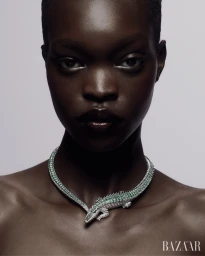 Close-up portrait of a Black woman wearing an emerald and diamond crocodile collar necklace against a pale grey studio background.
