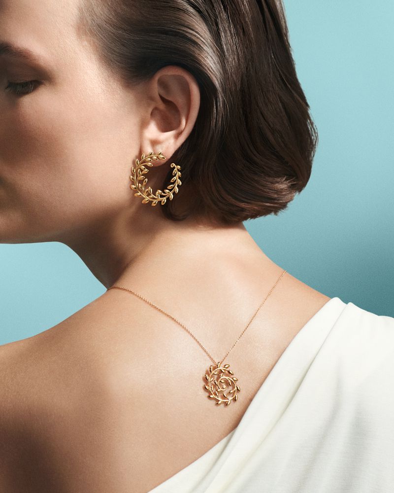 Profile shot of a woman showcasing gold hoop earrings and a matching necklace against a blue background in a fashion advertisement.