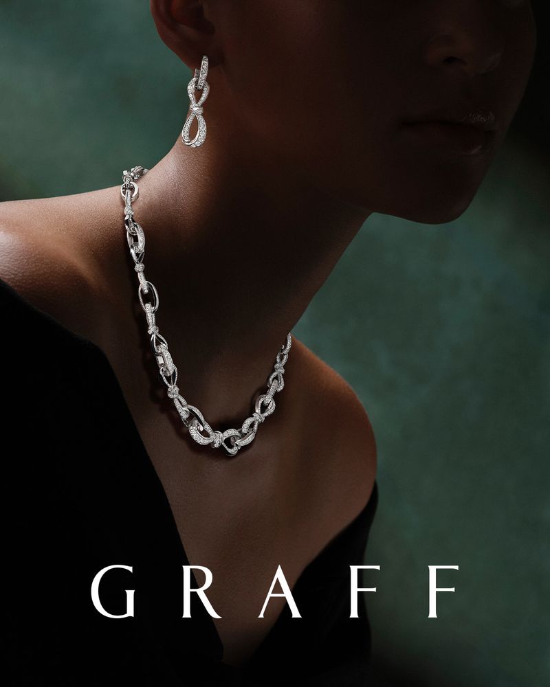 Close-up of a model wearing a Graff diamond necklace and earrings set against a dark teal background, showcasing jewelry.
