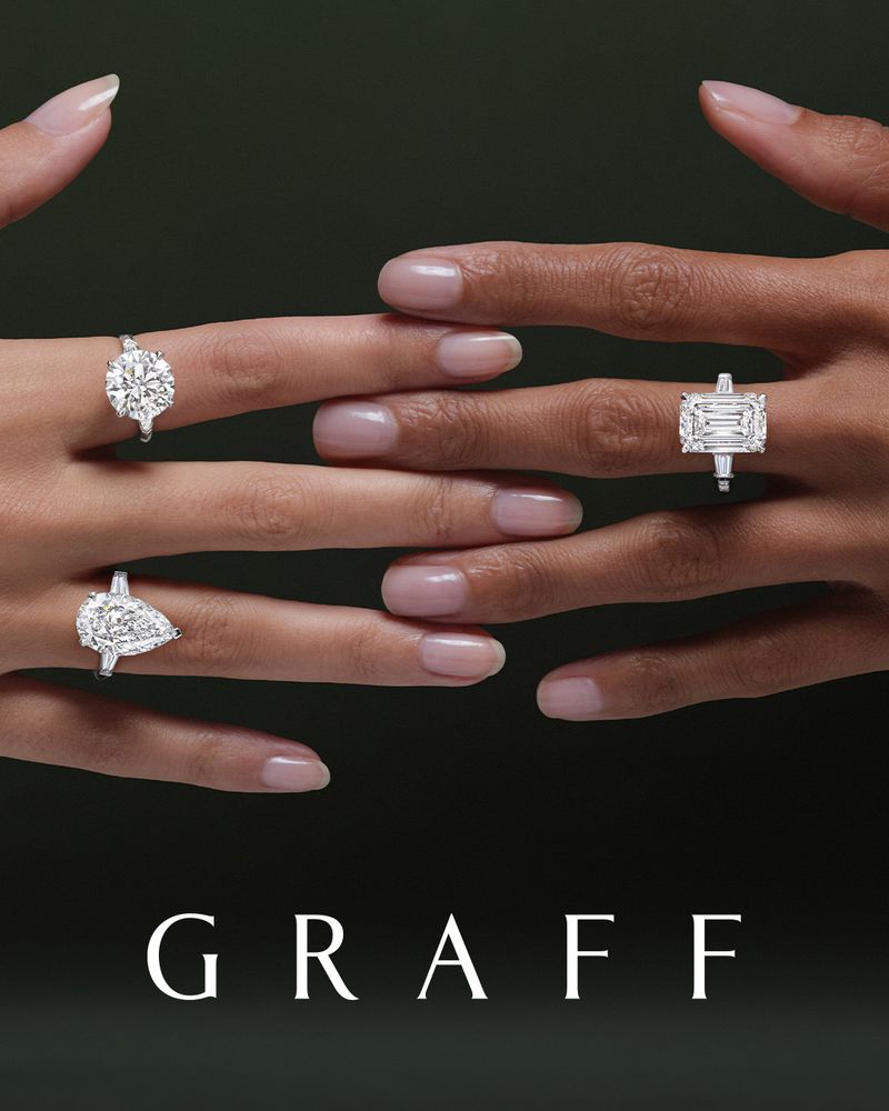 Close-up of two people of different skin tones displaying four diamond rings with silver bands against a dark green background.