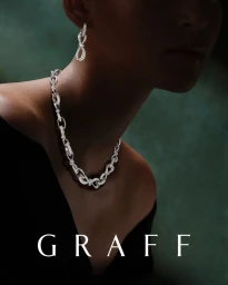 Model wearing an intricate diamond chain necklace and matching drop earring in low-key lighting for Graff.