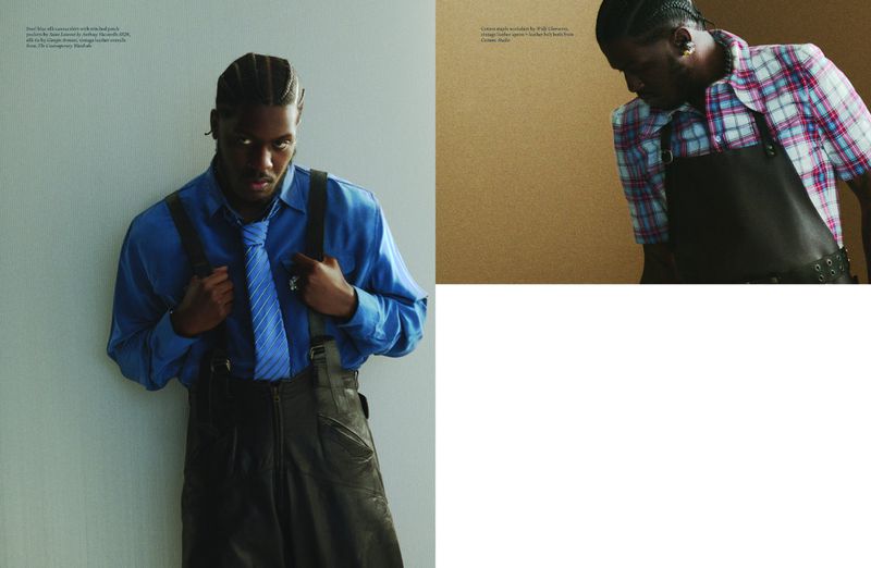 Editorial fashion shot of a Black male model wearing a blue silk shirt, striped tie, leather skirt and suspenders with a neutral backdrop.