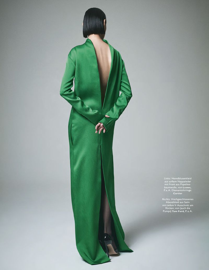 A model from the back wearing a long green dress with a plunging open back against a grey studio backdrop.