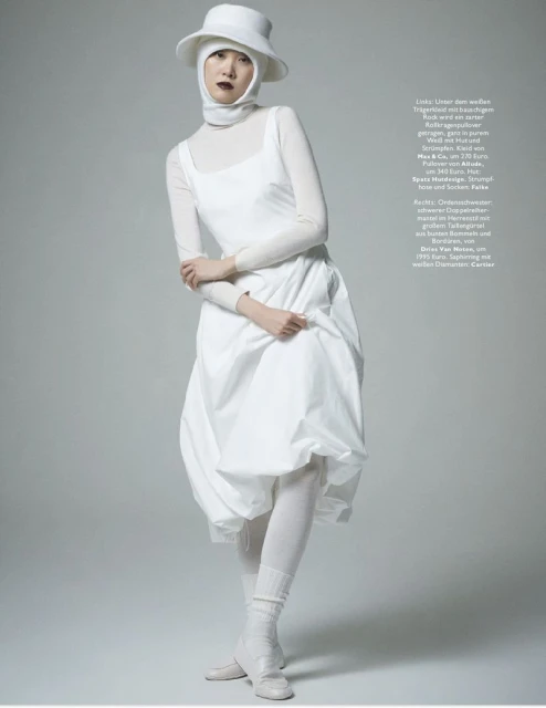 A fashion shot features an Asian woman in an all-white ensemble, including a dress, hat, and tights, standing in a light grey studio setting.