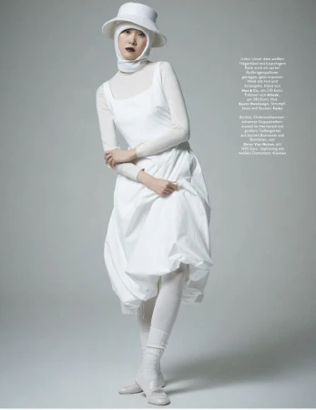 A fashion shot features an Asian woman in an all-white ensemble, including a dress, hat, and tights, standing in a light grey studio setting.