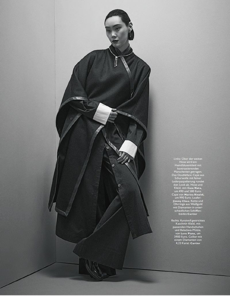 Model leaning against a corner wearing a dark coat with white cuffs and trousers for Madame Germany Sacre Coeur editorial